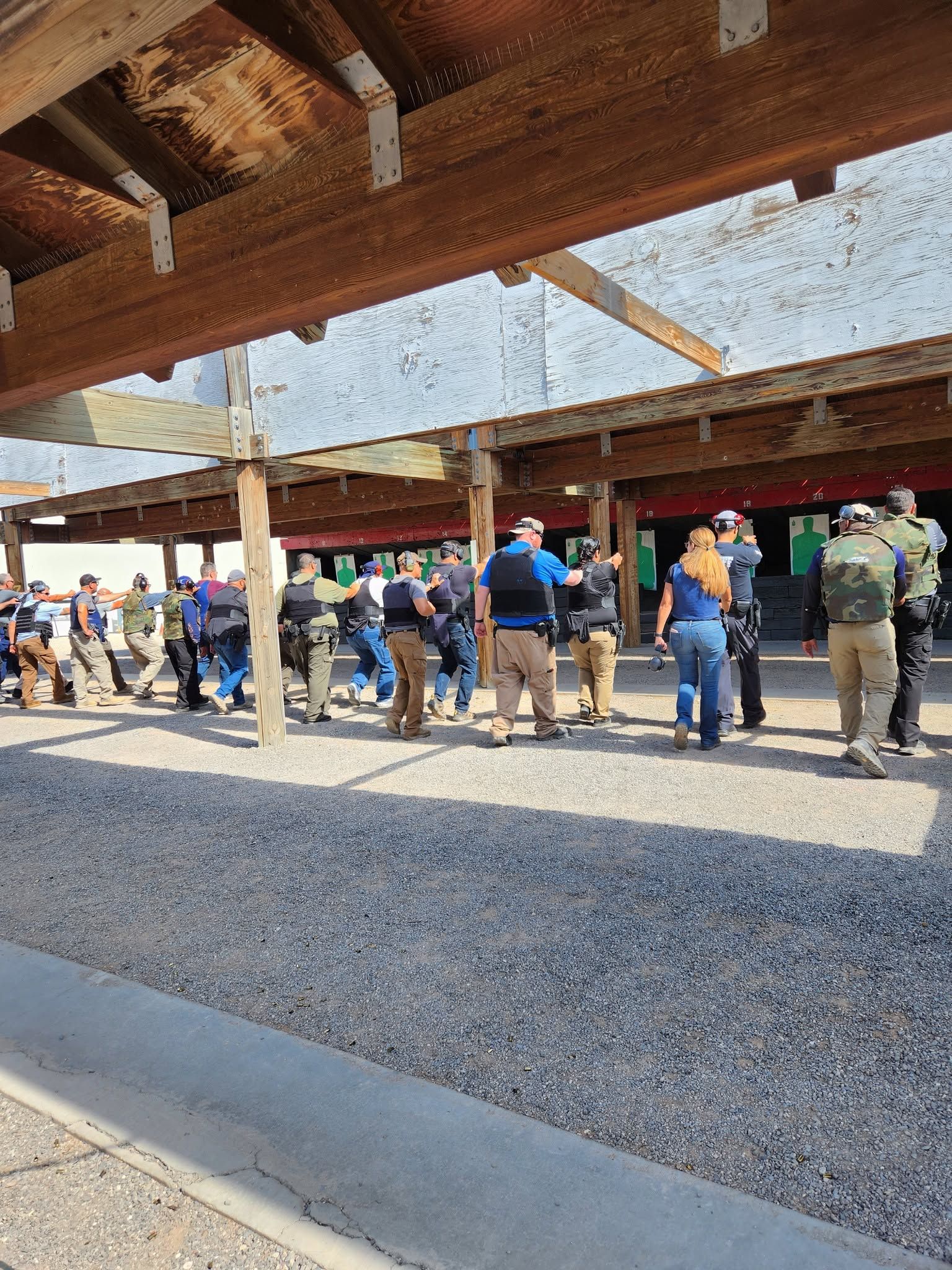 A line of officers from several agencies on a covered range, weapons up, working a drill together.